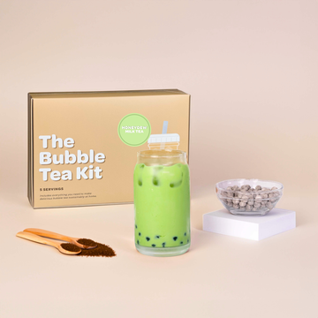 Bubble tea kit with honeydew milk tea drink, packaging, and ingredients on a beige background