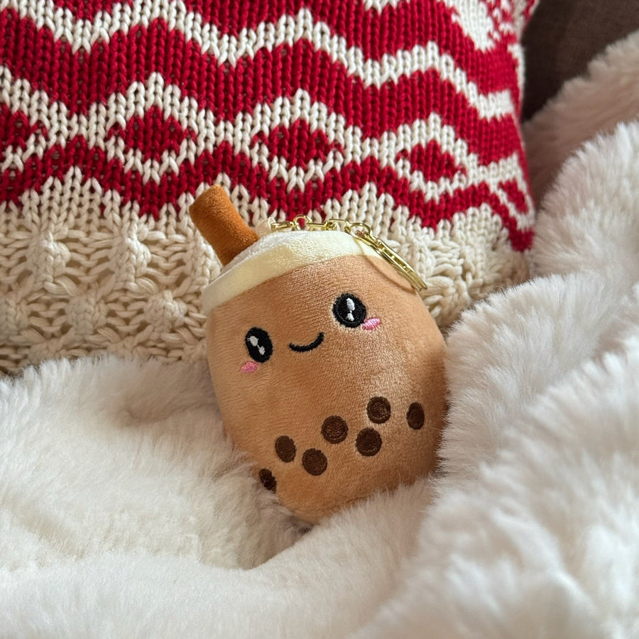 Plush toy resembling a boba drink on a fluffy white surface with a red and white patterned fabric in the background.