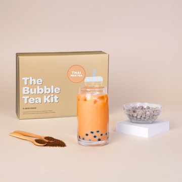 Bubble tea kit with a glass of bubble tea, tapioca pearls, and packaging on a beige background