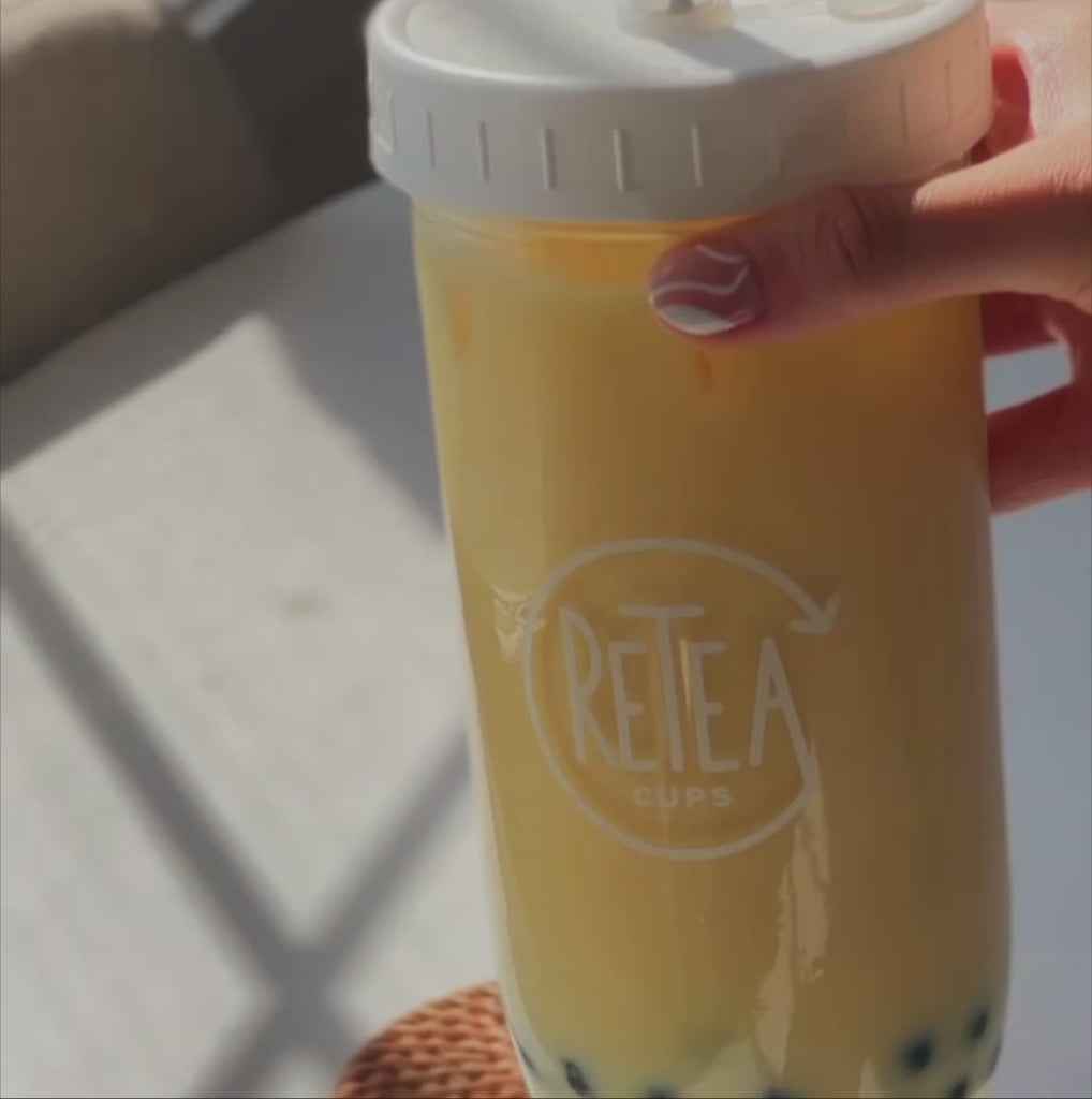 Video: Mango milk tea package unboxing reveals recyclable paper packaged creamer powder, dark brown sugar, mango milk tea powder, uncooked tapioca. 3 tablespoons of mango milk tea powder poured into clear, glass reusable Retea cup, add one tablespoon of lactose-free creamer, add 250 milliliters of hot water, stir with spoon until well mixed, add 250 milliliters of ice, put on non-leak plastic lid and shake until milk tea cools, add cooked tapioca, stir with silver reusable metal bubble tea straw